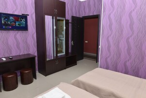 A hotel room with a bed, a desk with a computer, a wardrobe, and a TV mounted on the wall.
