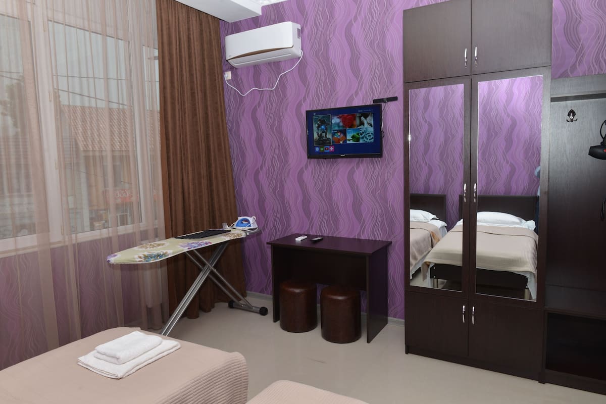 A hotel room with a bed, a desk with a computer, a TV, and a window with curtains.