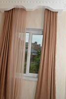 A window with beige curtains, a view of a cityscape, and a patterned wall.