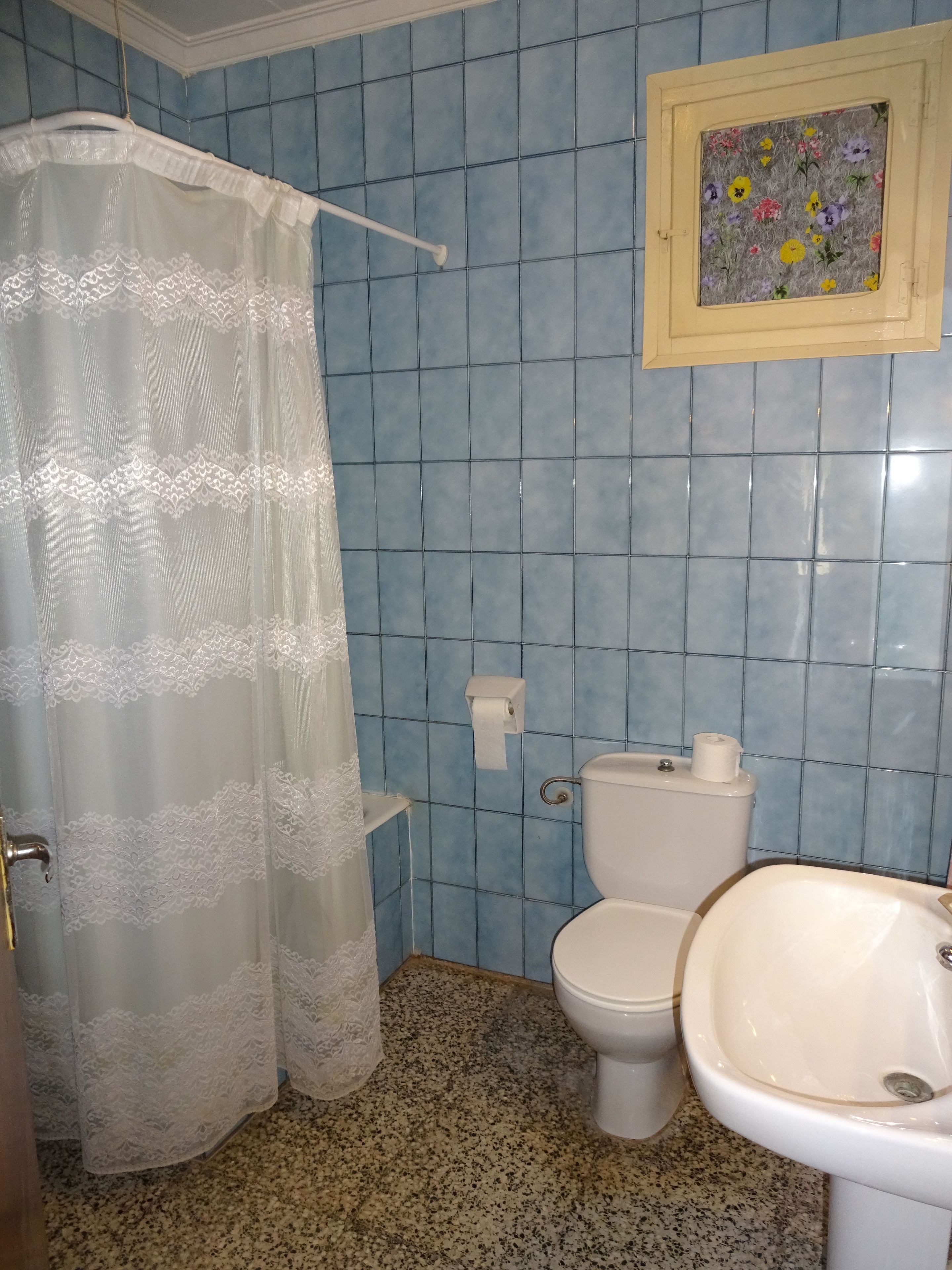 Un baño con azulejos azules, un inodoro, un lavabo y una cortina de ducha.