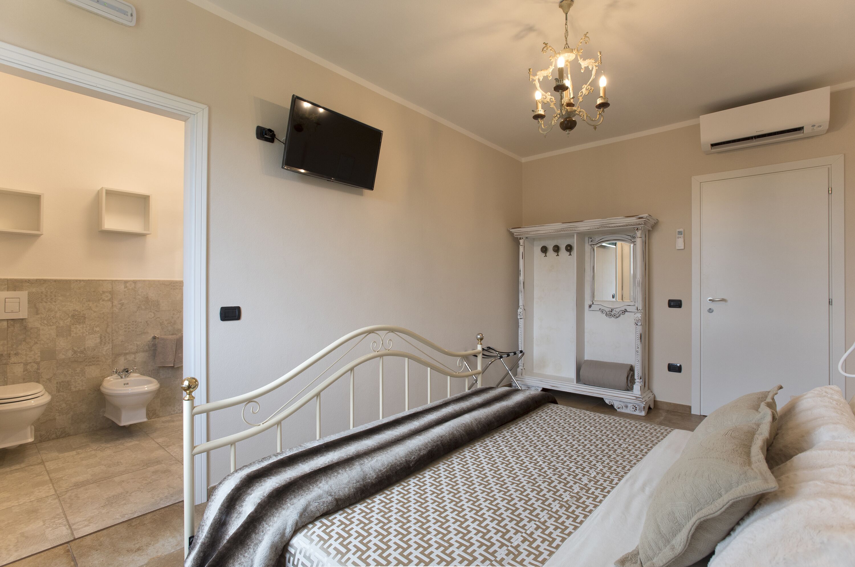 A bedroom with a bed, a television mounted on the wall, a wardrobe, and a mirror.