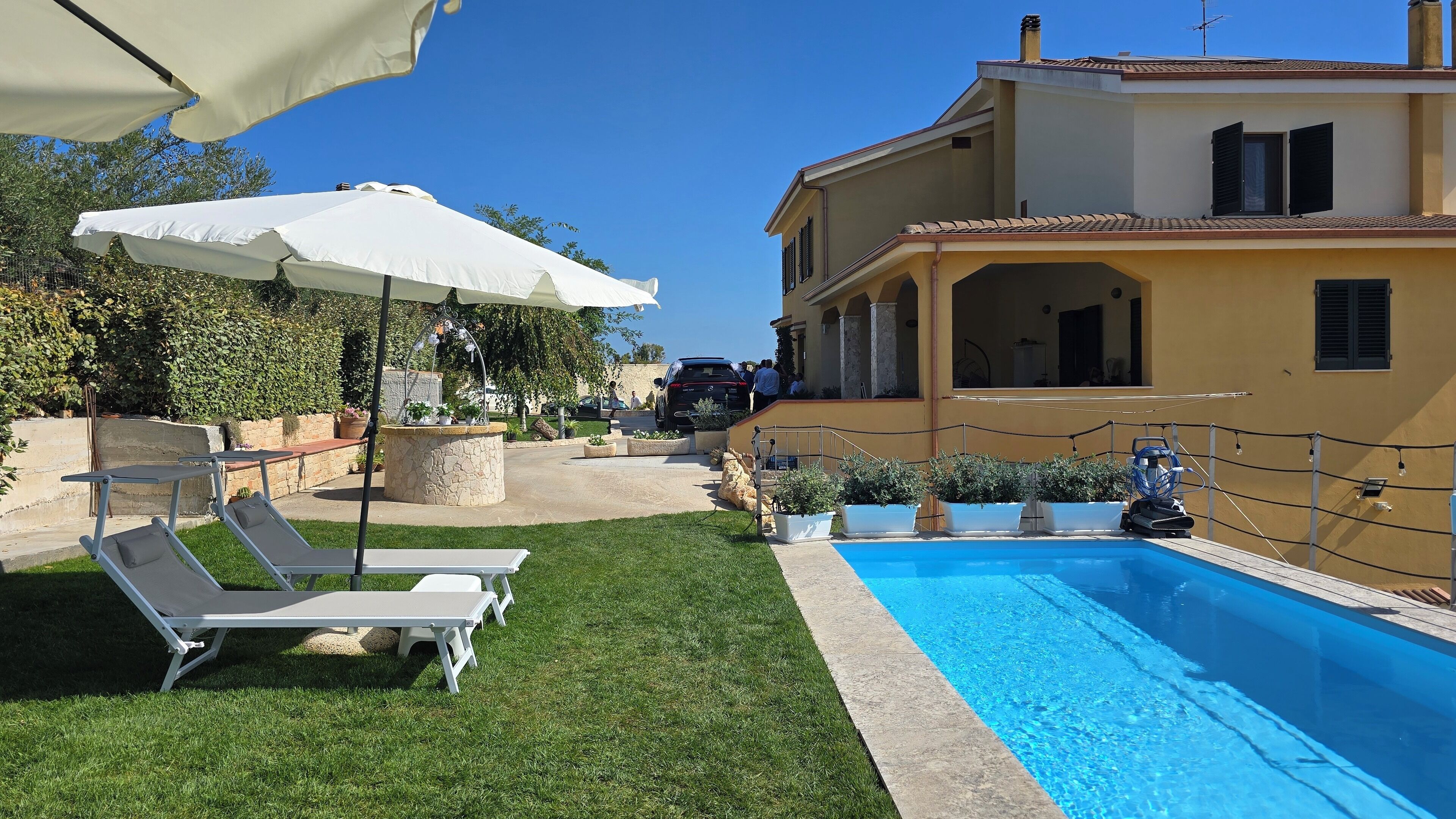 Zona de piscina con sillas de descanso, una fuente de piedra y una piscina azul cristalina.