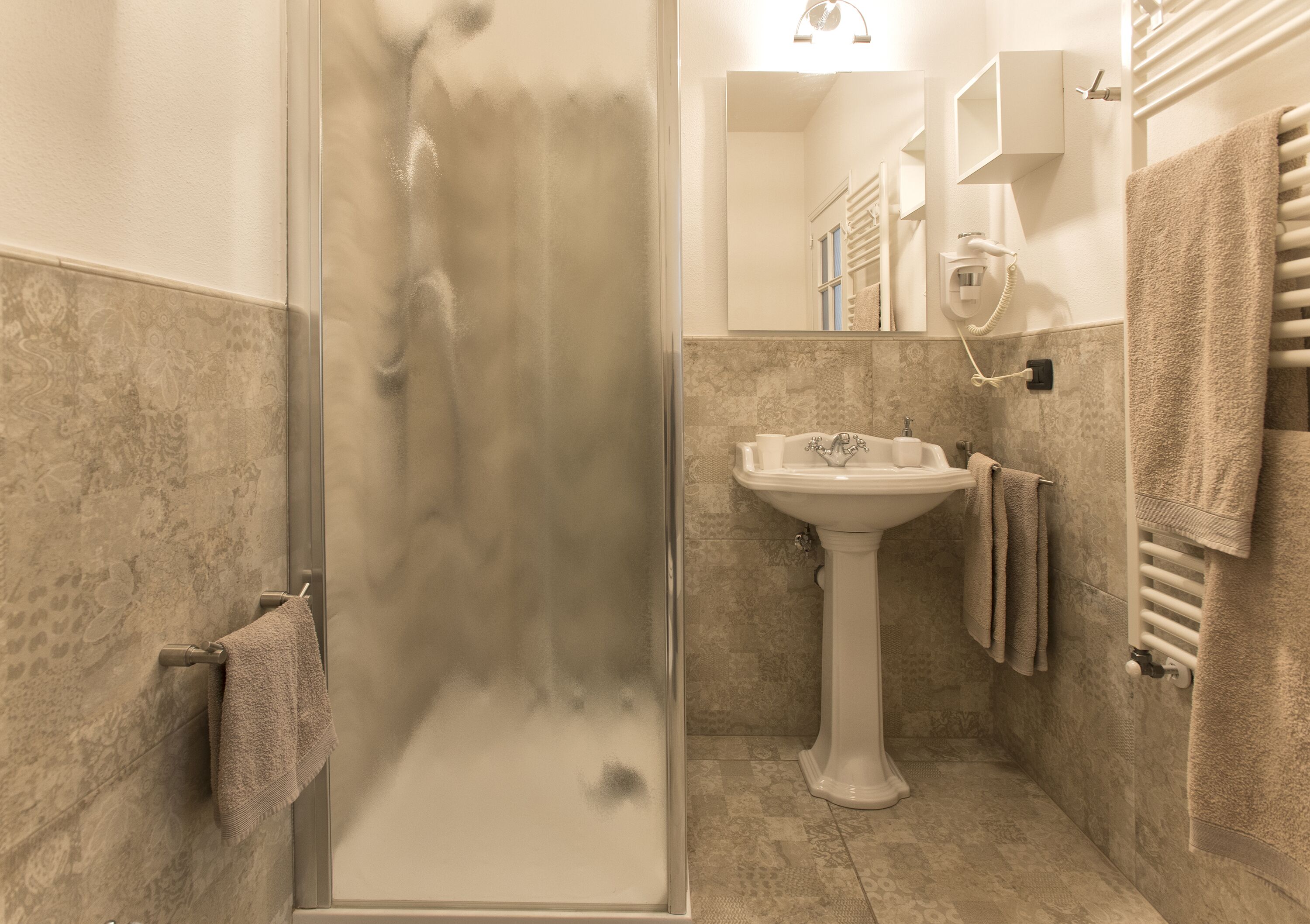 A bathroom with a glass shower enclosure, a pedestal sink, and a towel rack.