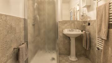 A bathroom with a glass shower enclosure, a pedestal sink, and a towel rack.