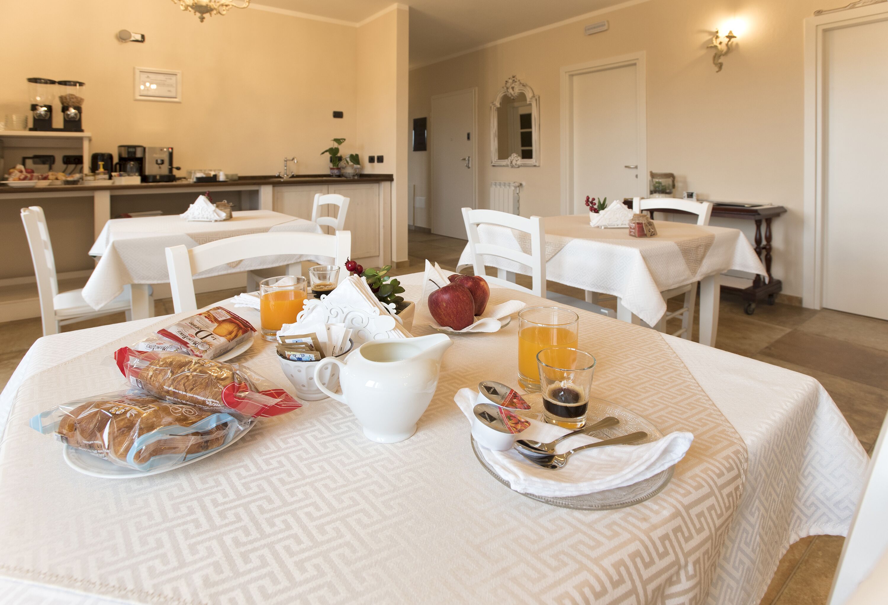 A dining area with tables set for breakfast, including bread, fruit, and beverages.
