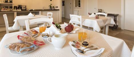 A dining area with tables set for breakfast, including bread, fruit, and beverages.