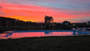 Una piscina al atardecer con vistas a un árbol y edificios lejanos.