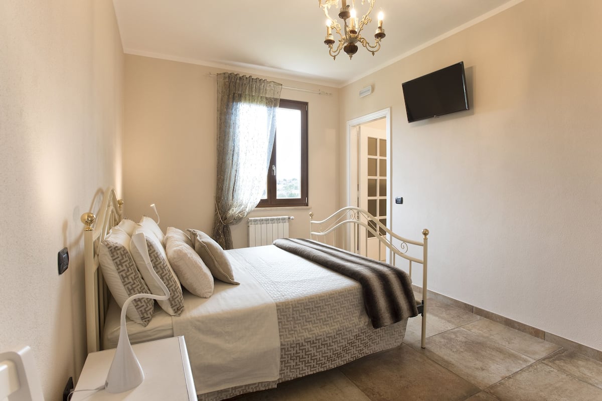 Une chambre à coucher avec un lit, un téléviseur fixé au mur, une fenêtre avec des rideaux et un radiateur.