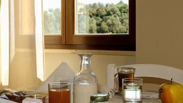 Ein Tisch mit einer Flasche, Gläsern, einem Einmachglas, einem Teller mit einem Apfel und einem Fenster mit Blick auf Bäume.