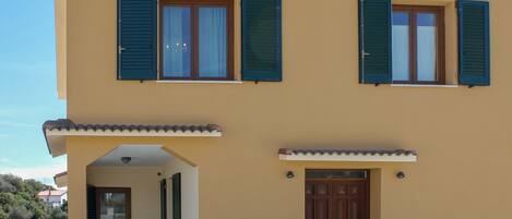 A two-story building with a balcony, a wooden door, and two windows with shutters.