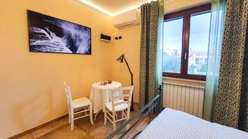 A hotel room with a bed, a small table with chairs, a painting on the wall, and a window with curtains.