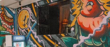 Et værelse med et farverigt muralmaleri, en rød sofa, et træskab og en minibar.