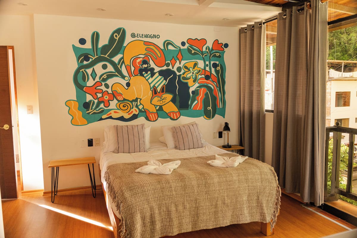 A bedroom with a large bed, a wooden bench, and a colorful mural on the wall.