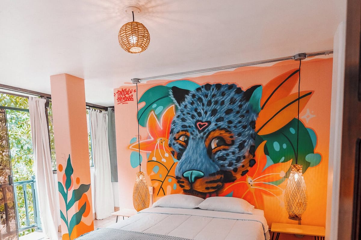 A bedroom with a large bed, a mural of a leopard's face, and a balcony with curtains.