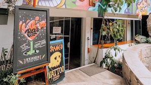 A building with a colorful mural, a tattoo studio sign, and a large plant. - Supertramp Hostel Machupicchu (Machu Picchu)