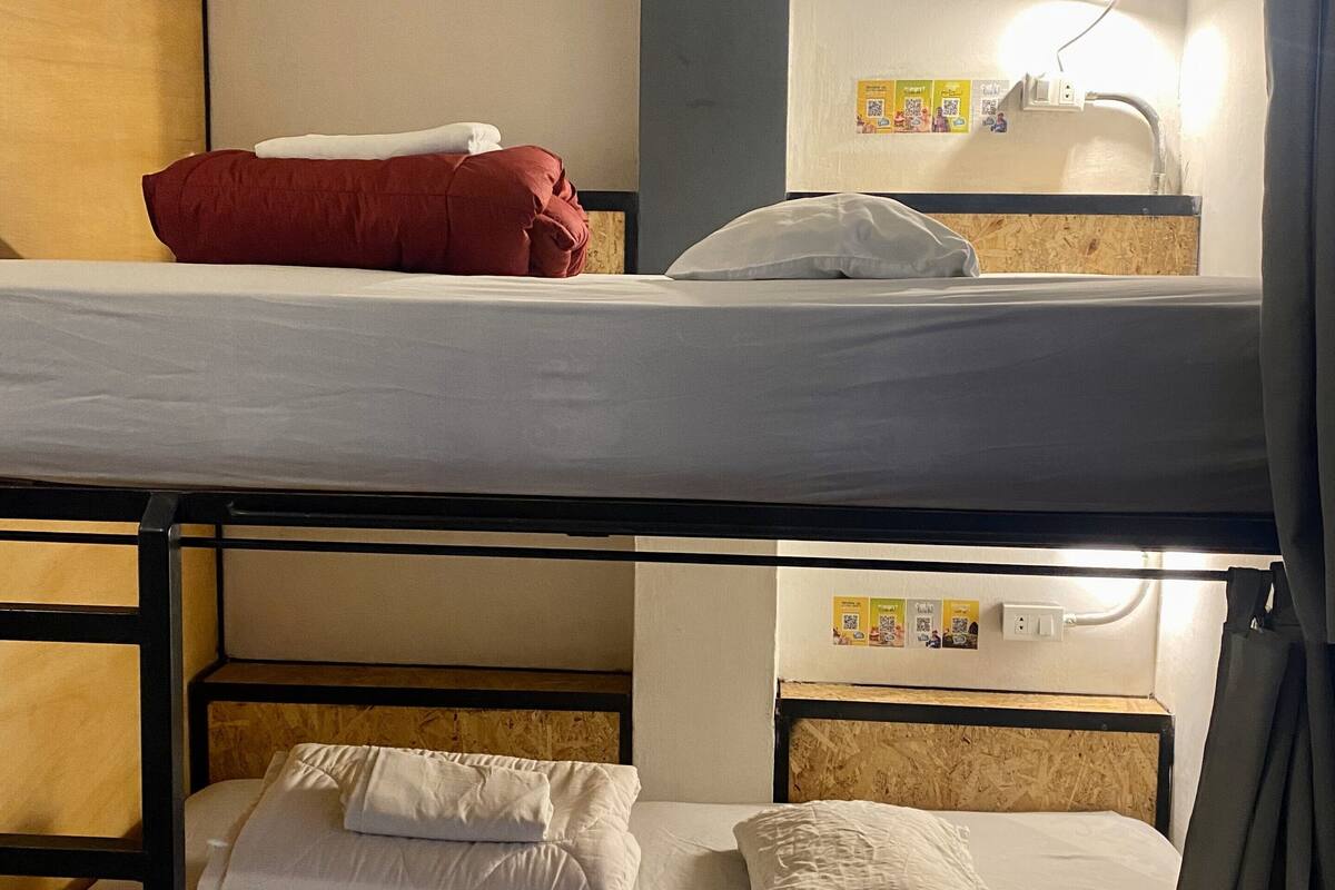 A bunk bed room with two beds, a wooden headboard, a wall-mounted light, and a bulletin board with QR codes.