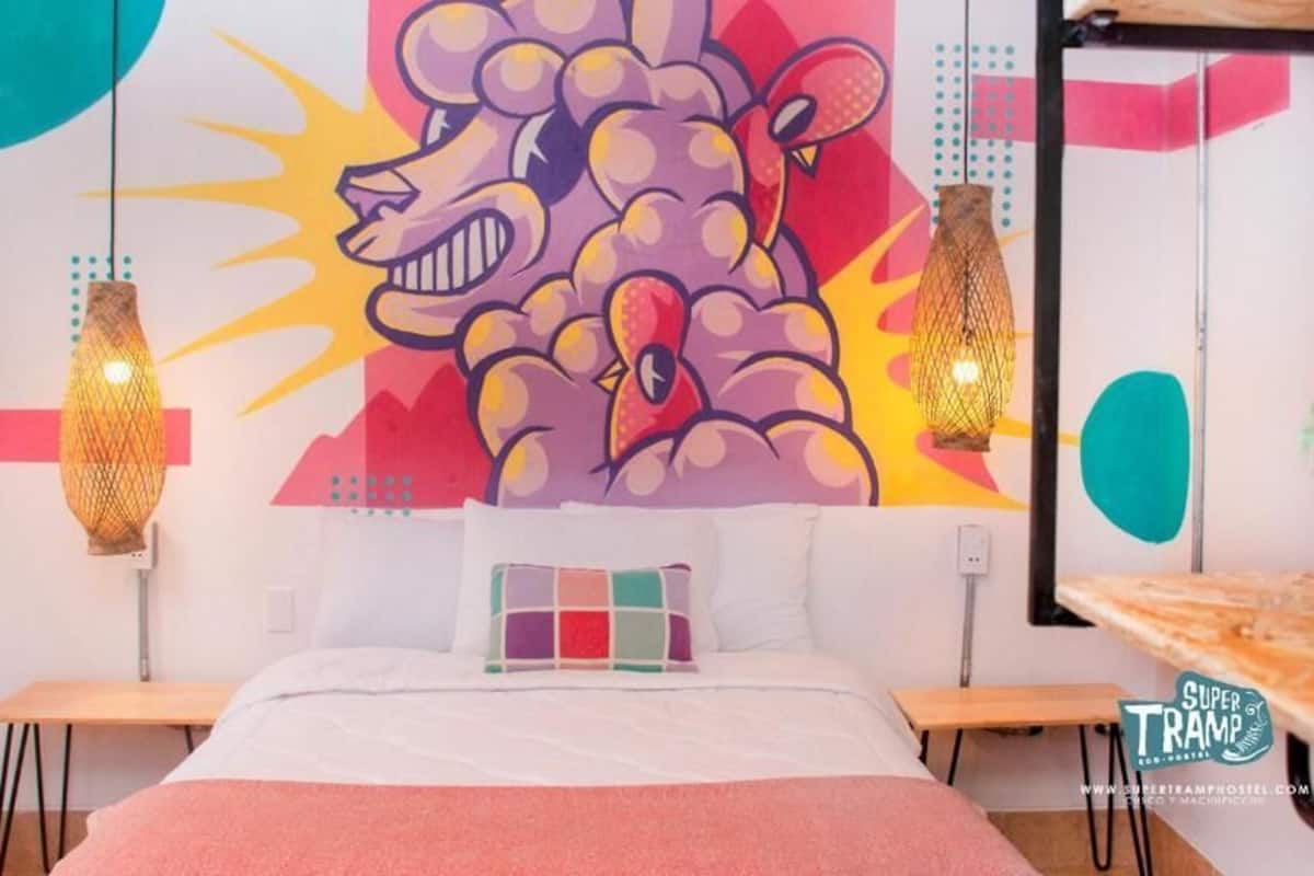 A bedroom with a bed, a colorful wall mural, two hanging lamps, and a small table with a bowl.