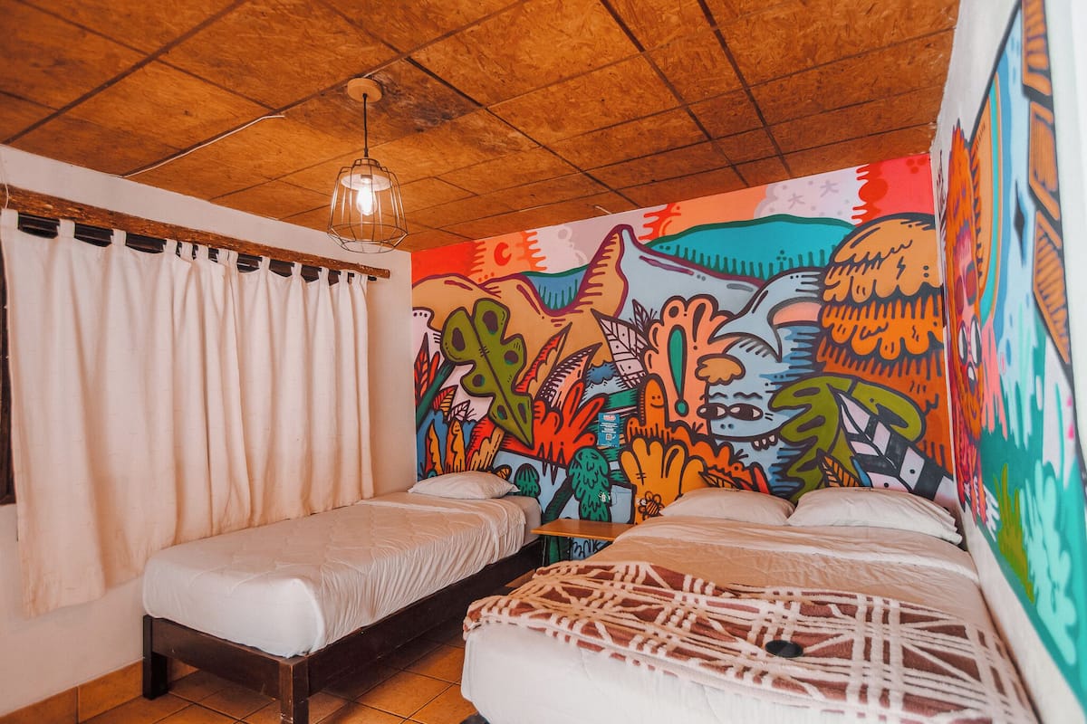 A room with two single beds, a wooden ceiling, and a colorful mural on the wall.