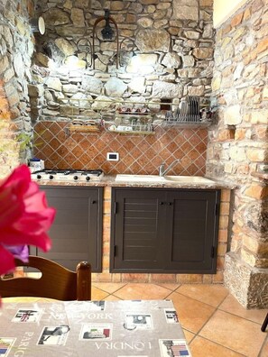 Una cocina con paredes de piedra, estufa a gas, pileta y alacenas.