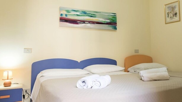 A hotel room with a bed, a nightstand, a lamp, and a painting on the wall. - Al Vicoletto (Taormina)