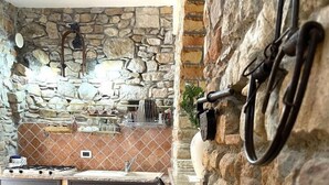 A kitchen with stone walls, a tiled floor, and a bar area with stools. - Al Vicoletto (Taormina)