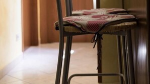 A chair with a patterned cushion in a room with a wooden door and a framed picture on the wall. - Al Vicoletto (Taormina)