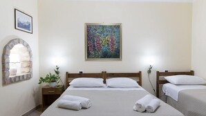 Een hotelkamer met twee bedden, een schilderij aan de muur, een potplant en een stenen boog.