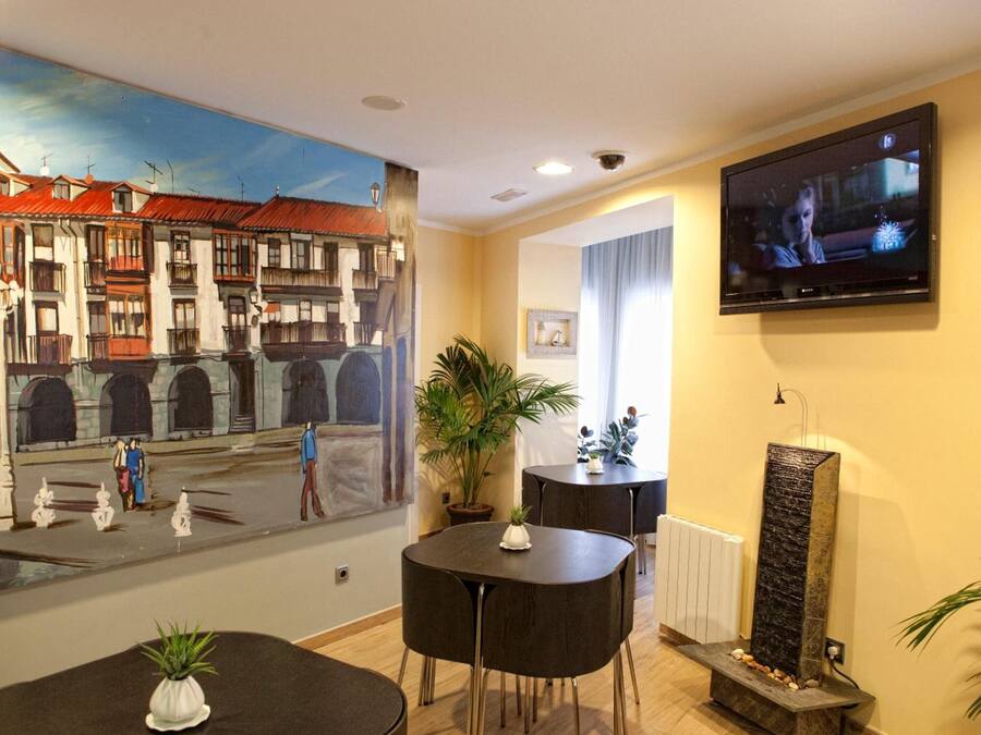 A hotel lobby with a large mural of a street scene, a flat-screen TV mounted on the wall, a reception desk, and a water feature.