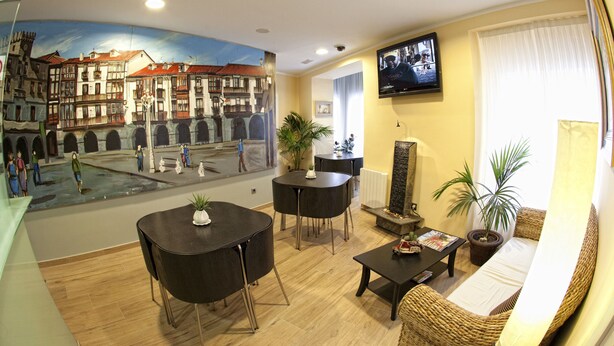 Una sala de estar con un mural de una ciudad europea, un comedor con una mesa y sillas, un sofá y una televisión en la pared.