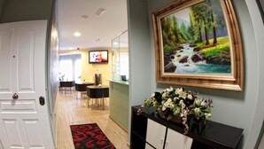 Un vestíbulo de hotel con un mostrador de recepción, un televisor montado en la pared, un cuadro de un arroyo en el bosque y un arreglo floral sobre una mesa consola.