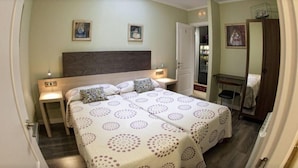 Habitación doble con dos camas, cabecera de madera, mesitas de noche con lámparas y un pequeño escritorio con silla.