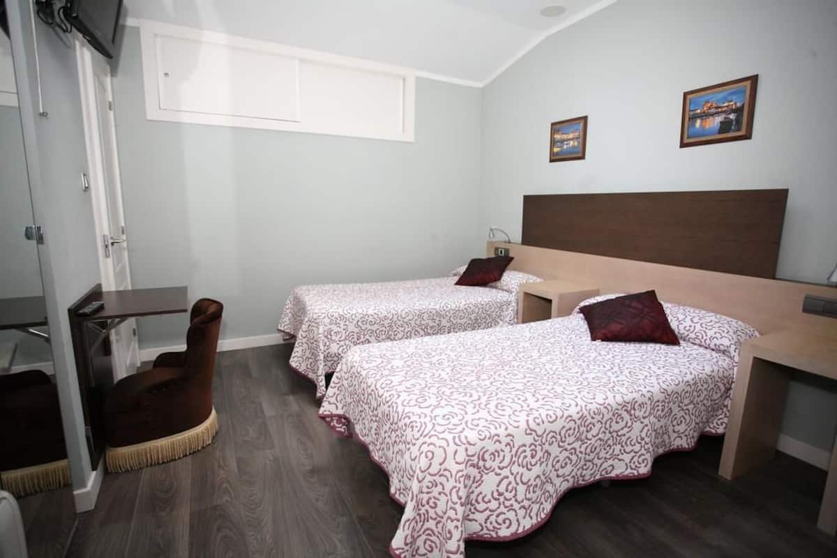A hotel room with two beds, a desk, a chair, and a TV.