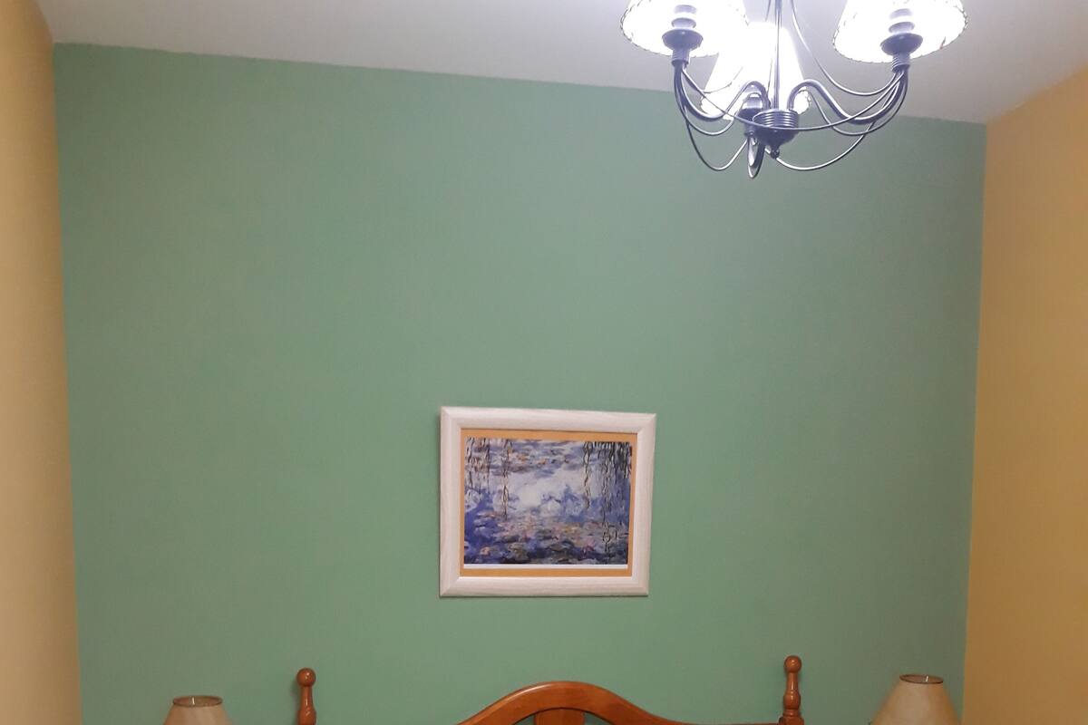 Un dormitorio con una cama, dos mesitas de noche, una araña y un cuadro en la pared.