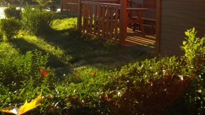 A wooden cabin with a porch, surrounded by greenery and a clear sky.