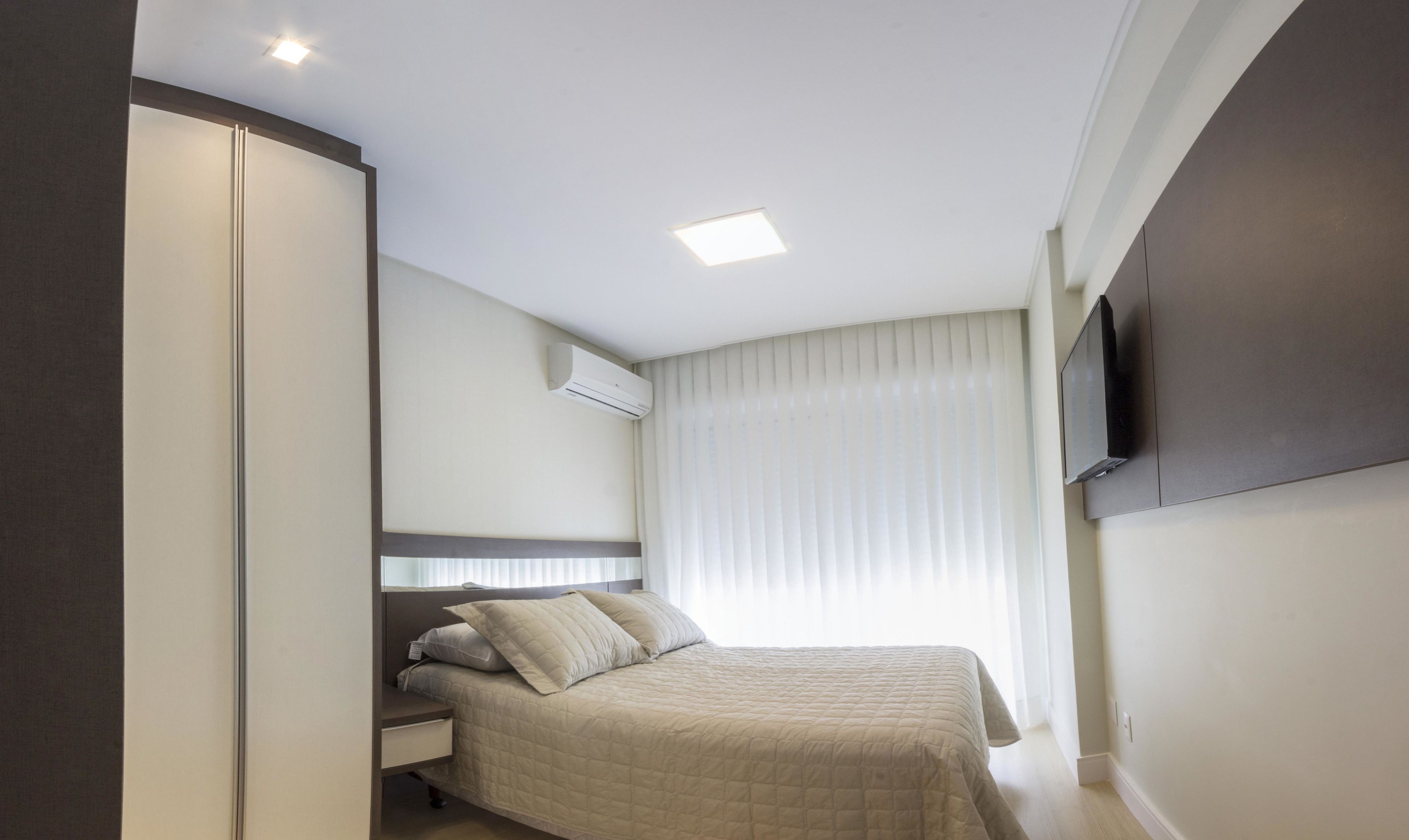 Una habitación de hotel con cama, televisor montado en la pared, armario y luz de techo.