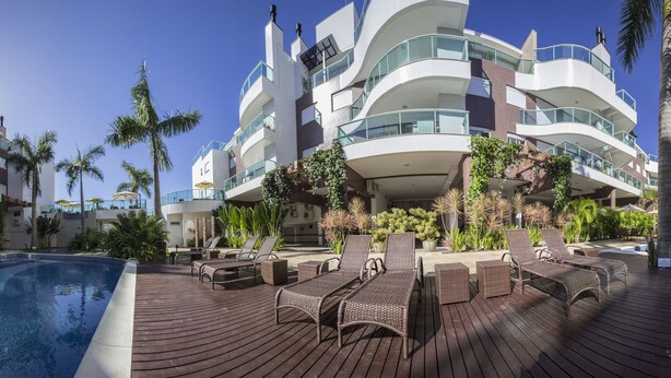 Un hôtel moderne doté de nombreux balcons, d’un espace piscine avec des chaises longues et de palmiers.