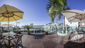 Une terrasse sur le toit avec des espaces salons extérieurs, une piscine et des palmiers.