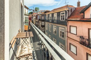 A narrow street with buildings on either side, balconies, and a wooden table with cushions. - North Star Flats - Ribeira & Cellars (Vila Nova de Gaia)