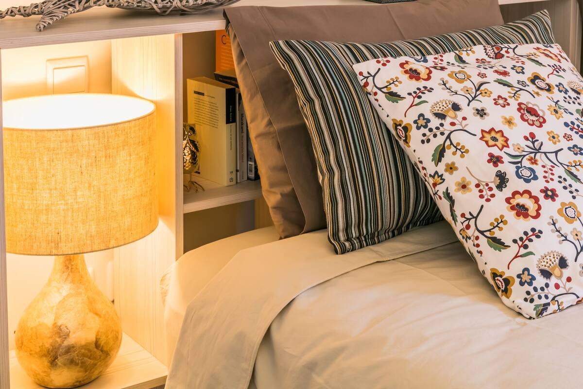 A neatly made bed with a floral pillow, a striped pillow, and a beige blanket.