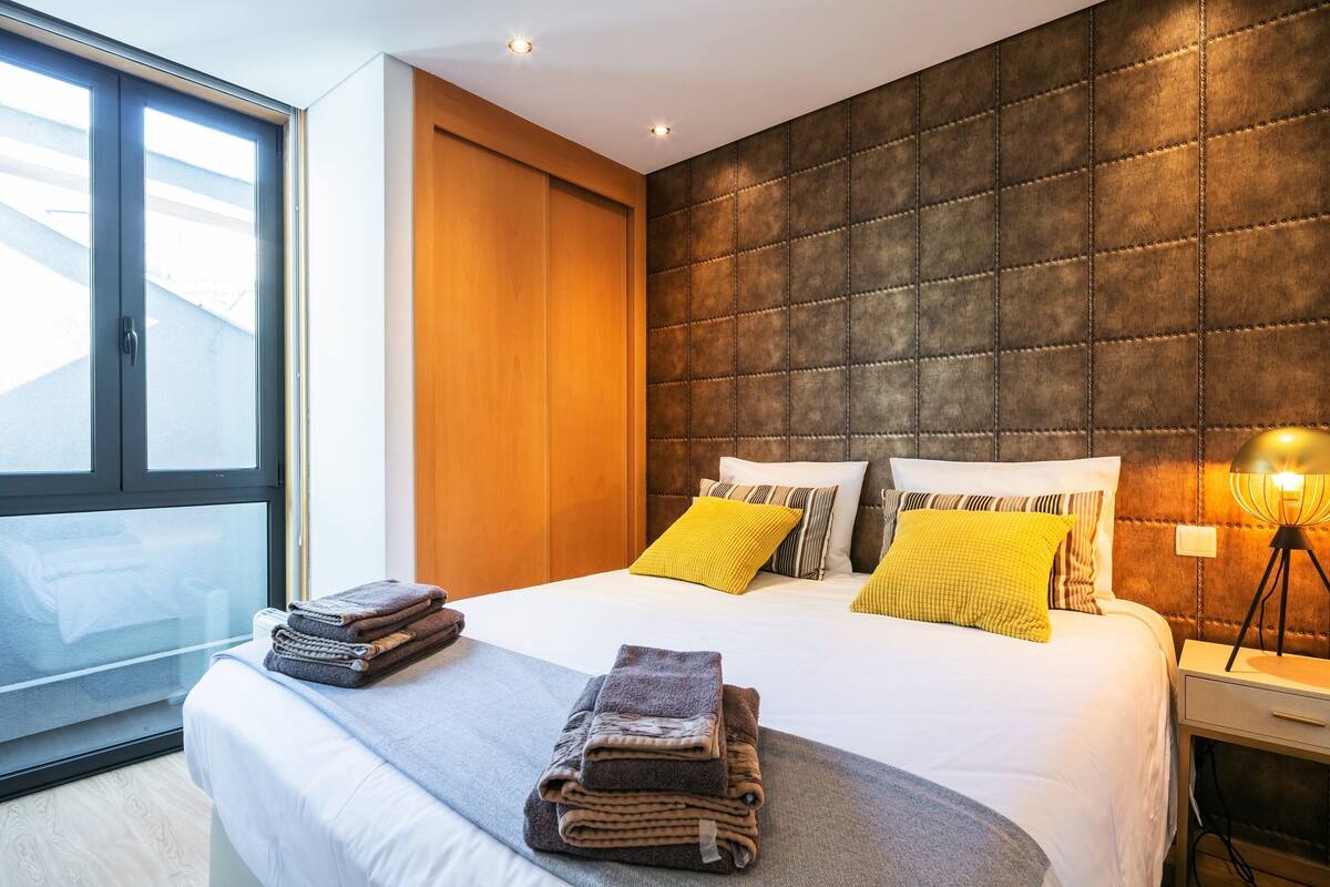 A modern hotel room with a large bed, a wooden wardrobe, and a large window.