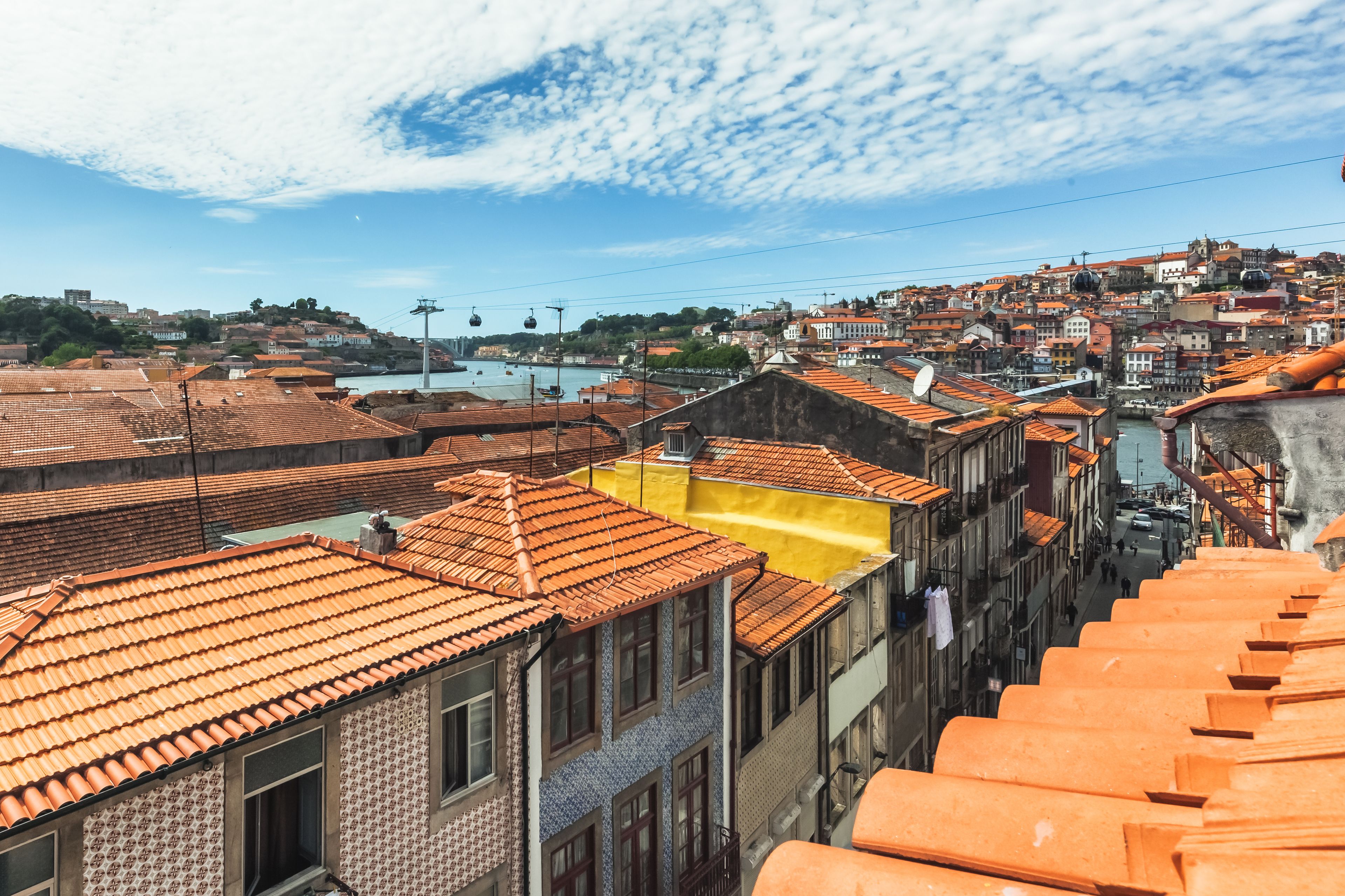 Paesaggio urbano con edifici a tetti in terracotta, un fiume e un sistema di funivia.