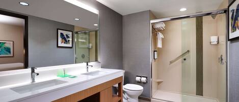 Une salle de bain moderne dotée de deux lavabos, de toilettes et d’une douche séparée par une paroi de verre.
