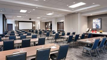 A conference room with multiple tables and chairs, a projector screen, and a presentation area.