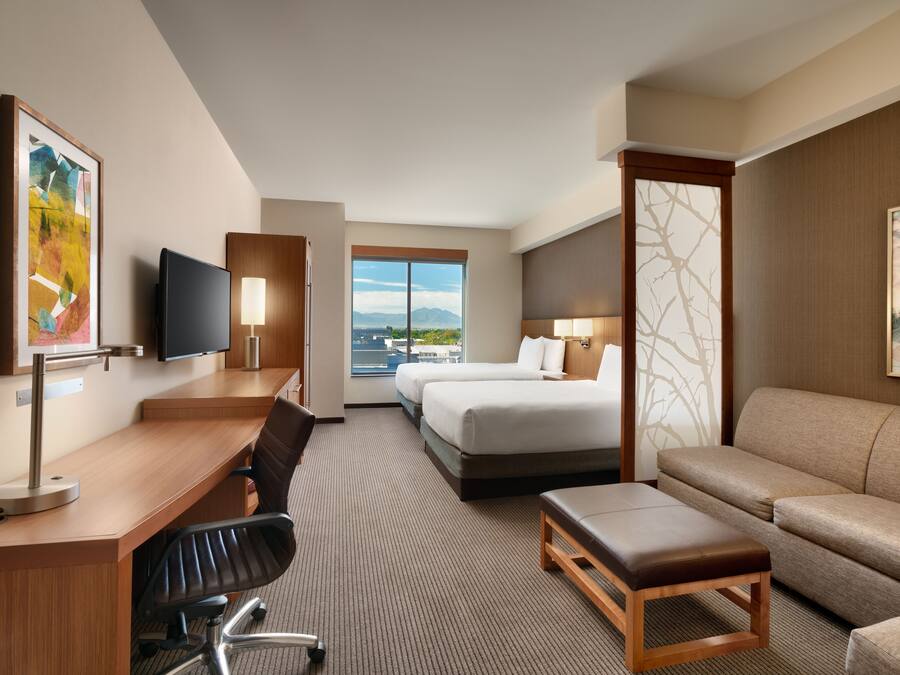 A hotel room with a desk, two beds, a sofa, and a TV.