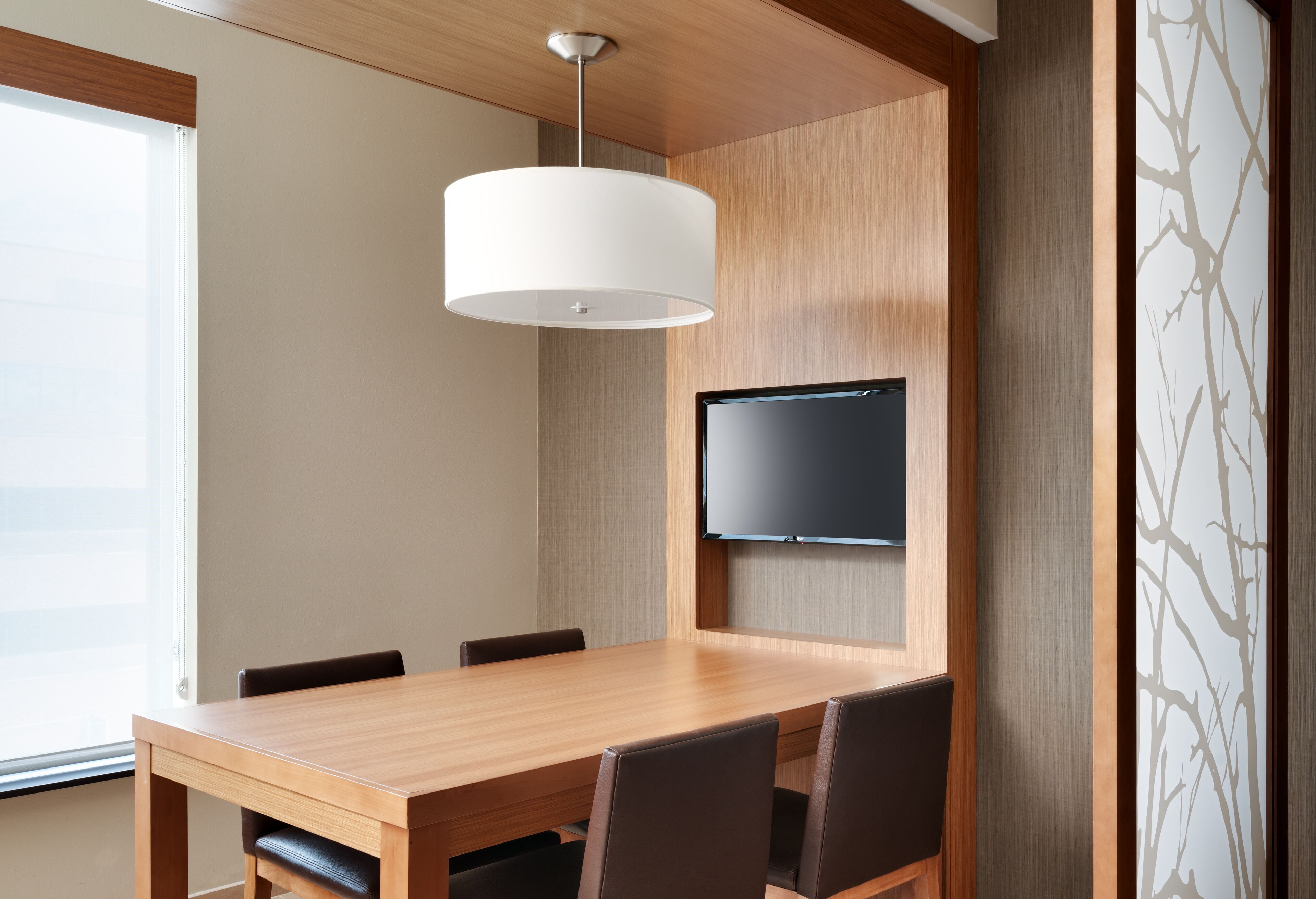 A conference room with a wooden table, chairs, a flat-screen TV, and a ceiling light fixture.