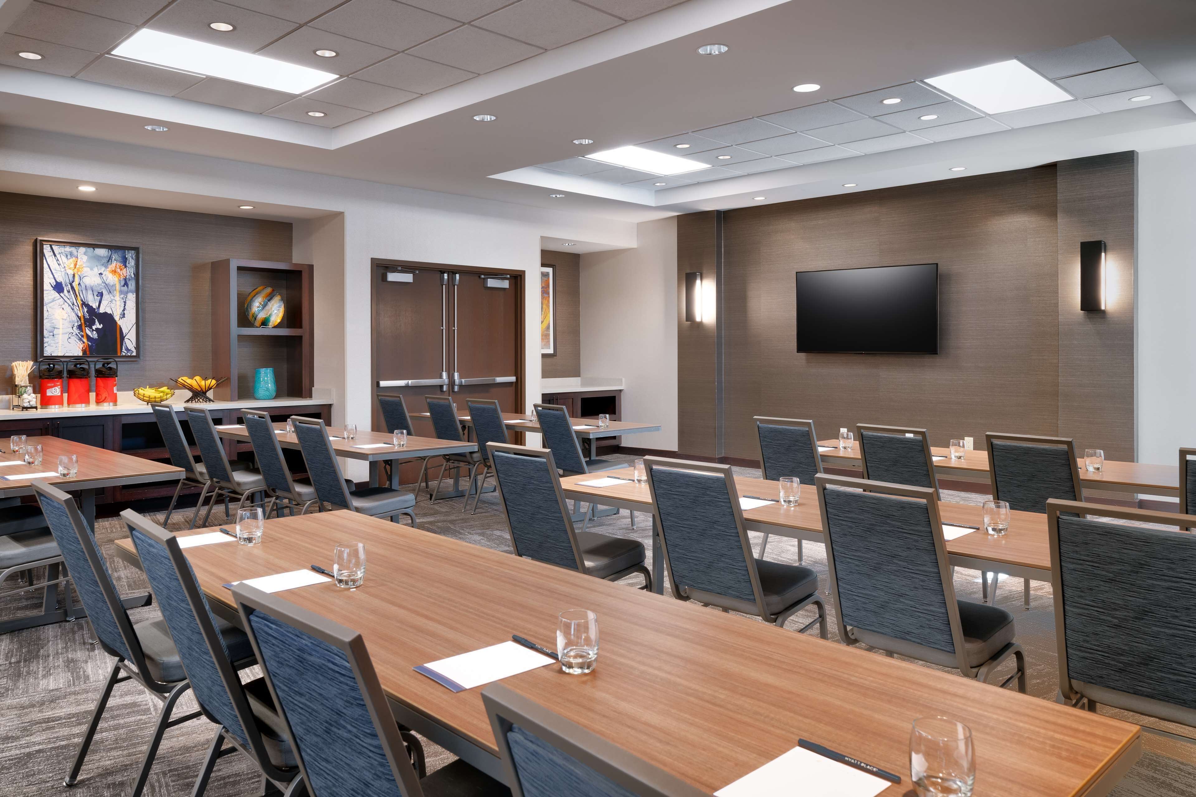 A conference room with multiple tables and chairs, a flat-screen TV mounted on the wall, and a reception area with artwork and a counter.
