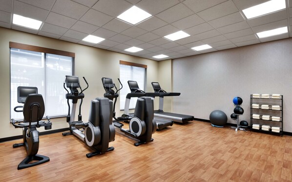 Un gimnasio con diversos equipos de ejercicio, incluyendo cintas de correr, elípticas y una máquina de remo.