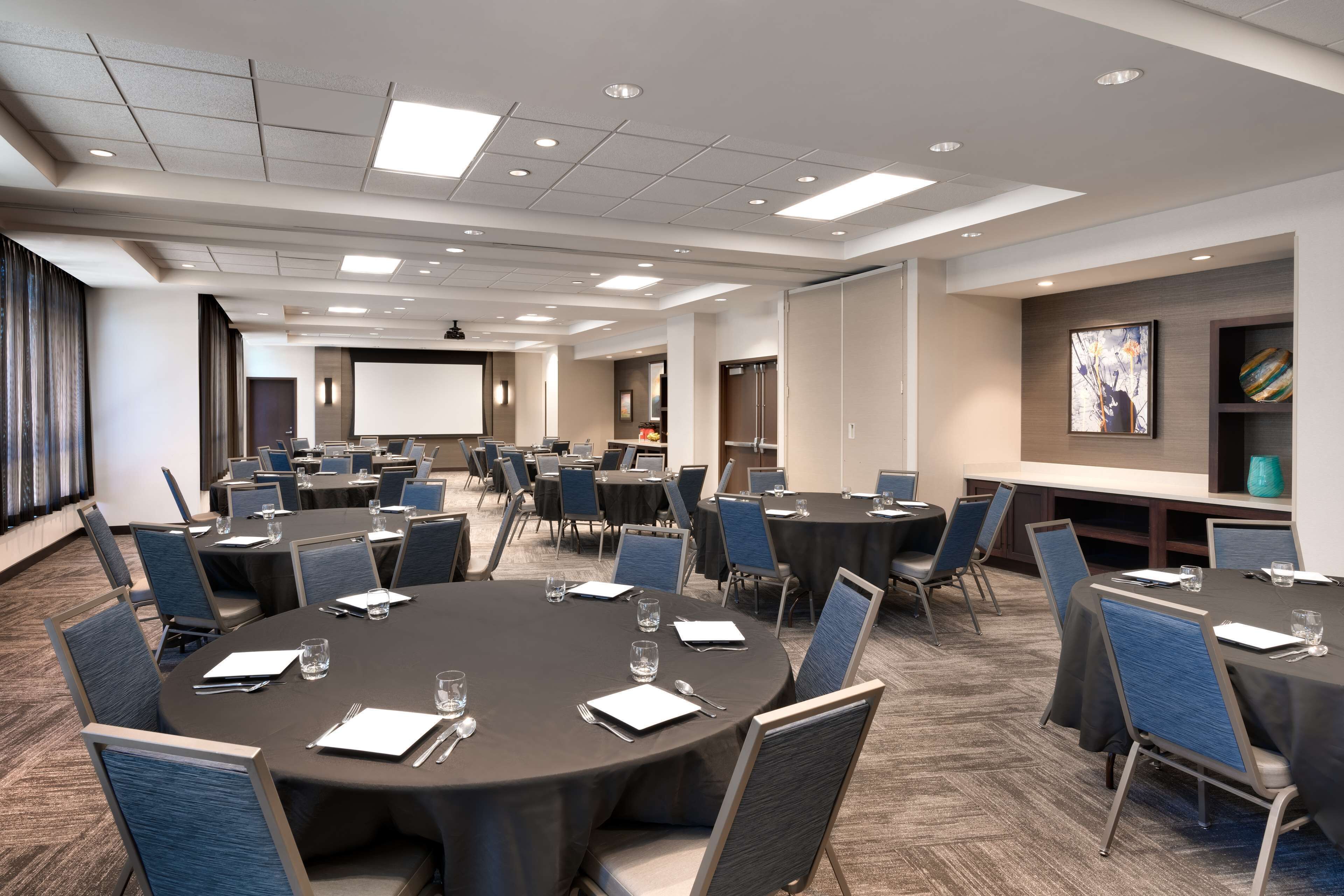 A conference room with multiple round tables, each set with chairs, glasses, and notepads.