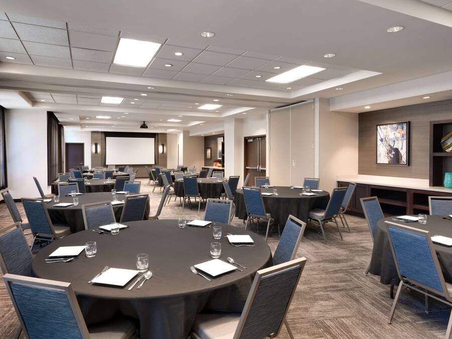 A conference room with multiple round tables, each set with chairs, glasses, and notepads.
