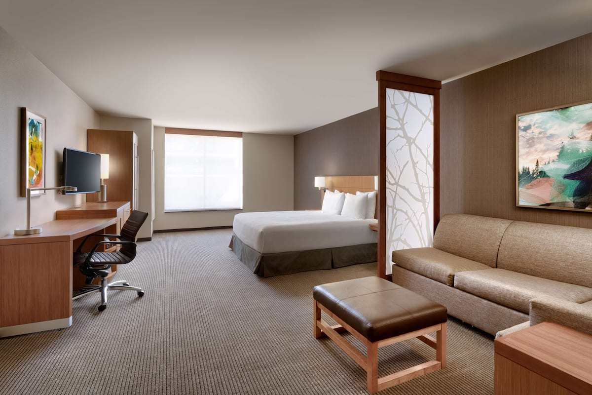 Ein Hotelzimmer mit Bett, Schreibtisch mit Stuhl, einer Couch, einem kleinen Tisch und einem Fernseher.